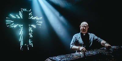 Padre Guilherme am DJ Pult mit Kreuz im Hintergrund