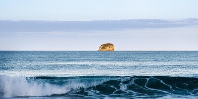 ein einsamer Felsen ragt als Insel aus dem Meer, Brandung spült gegen den Betrachter