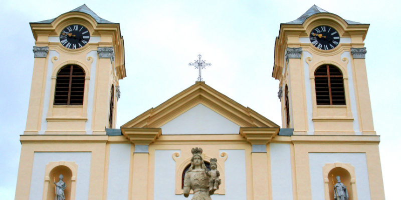Blick auf die Frontfassade der Basilika zur Unbefleckten Empfängnis in Loretto. Im Vordergrund befindet sich die steinerne Marienfigur, die auf dem Torbogen des Portals der Vorhofmauer steht. Sie ist eine der vielen Mariendarstellungen, die die Besuc