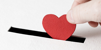 Eine Hand steckt ein Herz aus Karton in den Schlitz einer Spendenbox.