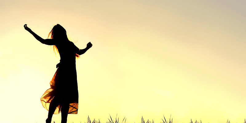 Eine Frau steht im Gegenlicht vor einem gelben Himmel und reckt die Arme jubelnd nach oben.